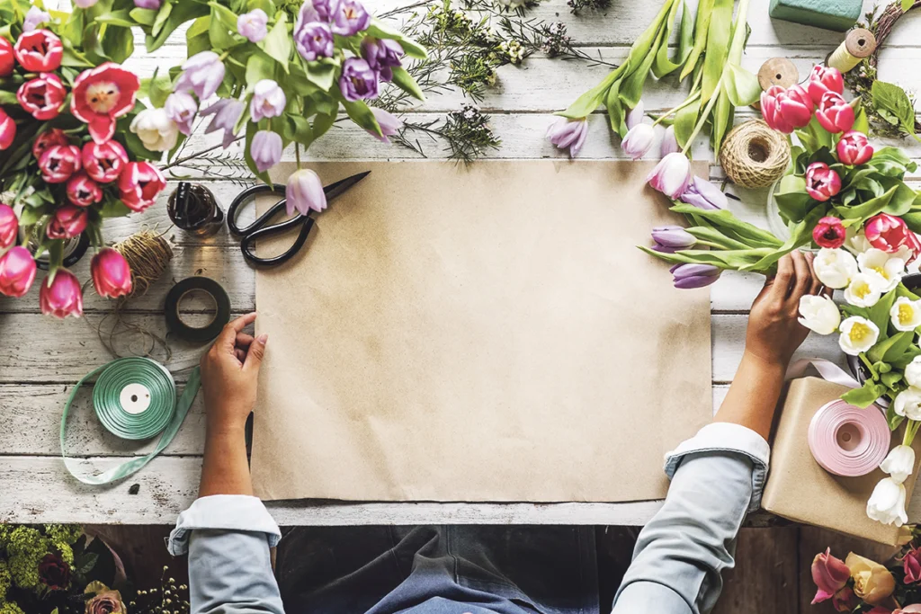 Handen op een werktafel vol tulpen, pakpapier, een schaar en linten
