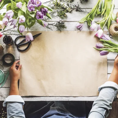 Handen op een werktafel vol tulpen, pakpapier, een schaar en linten